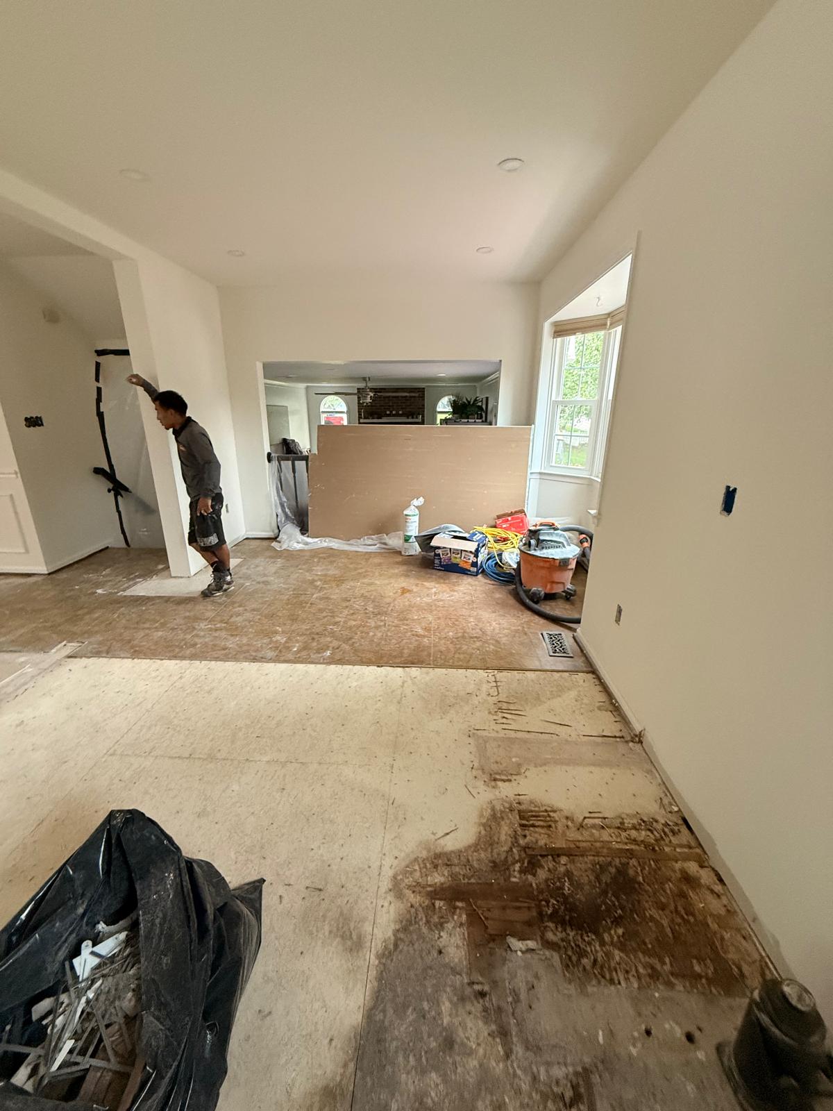 Kitchen and dining area with worn flooring pulled up to the bare subfloor and renovation materials staged along the wall