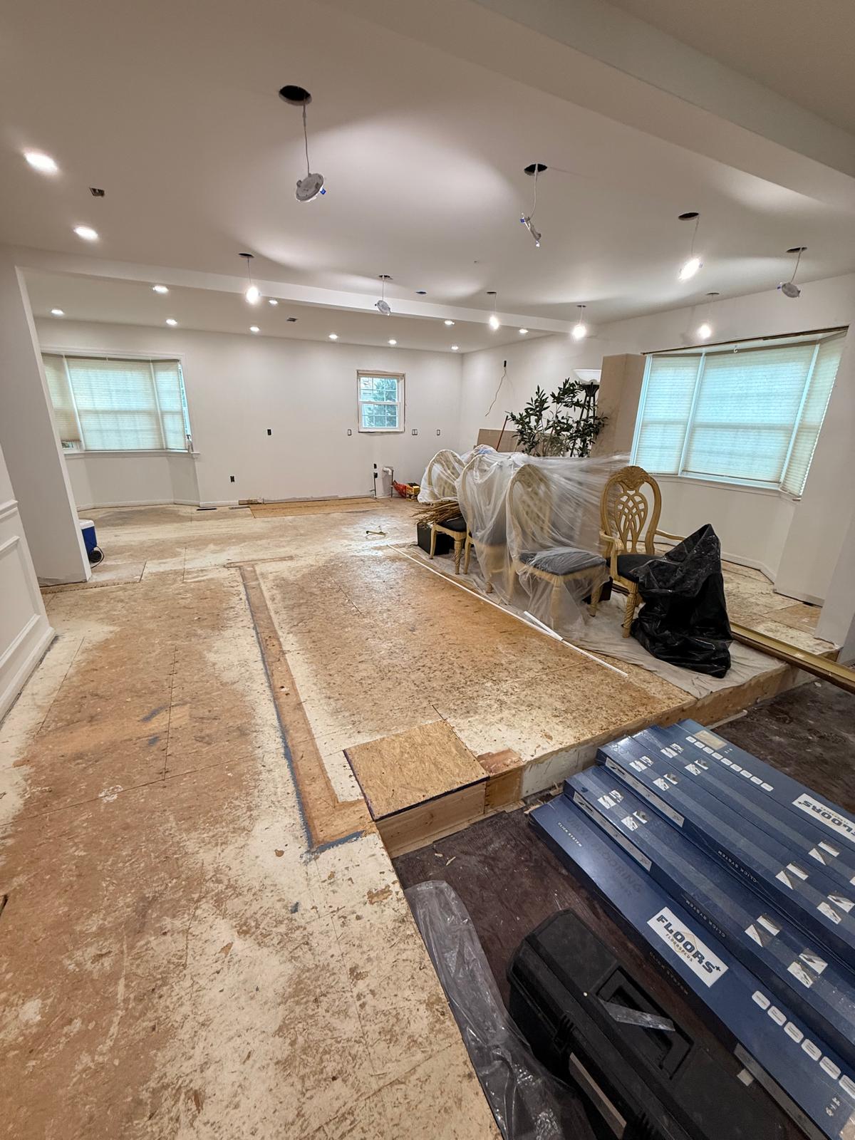 Open-plan living, dining and kitchen area stripped down to bare plywood decking with new click-lock flooring boxes staged