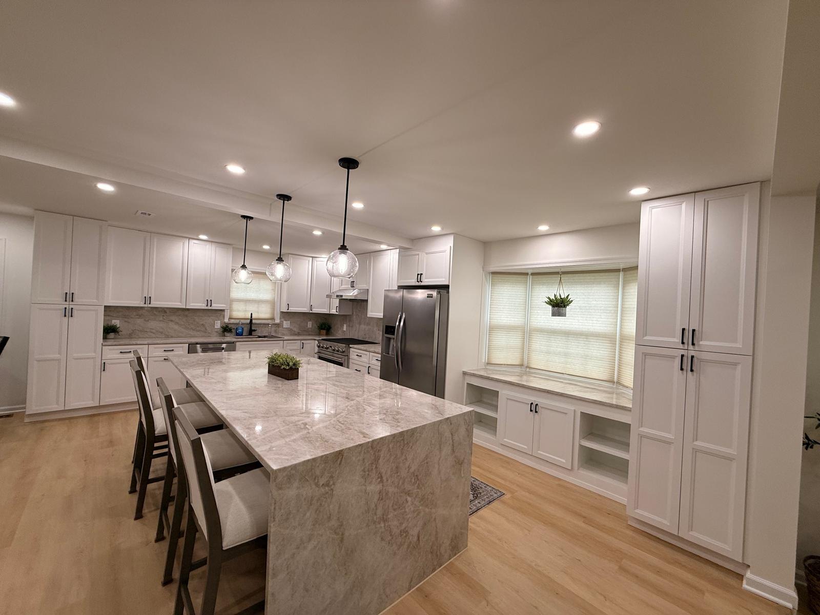 Wide view of a finished kitchen with a marble waterfall-edge island, four upholstered stools, glass globe pendants and stainless steel appliances