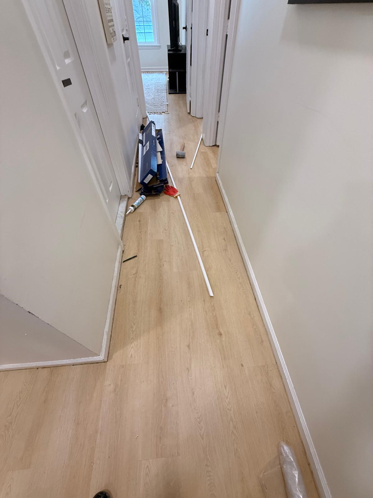 Hallway with newly laid light wood-tone plank flooring and baseboard trim being fitted