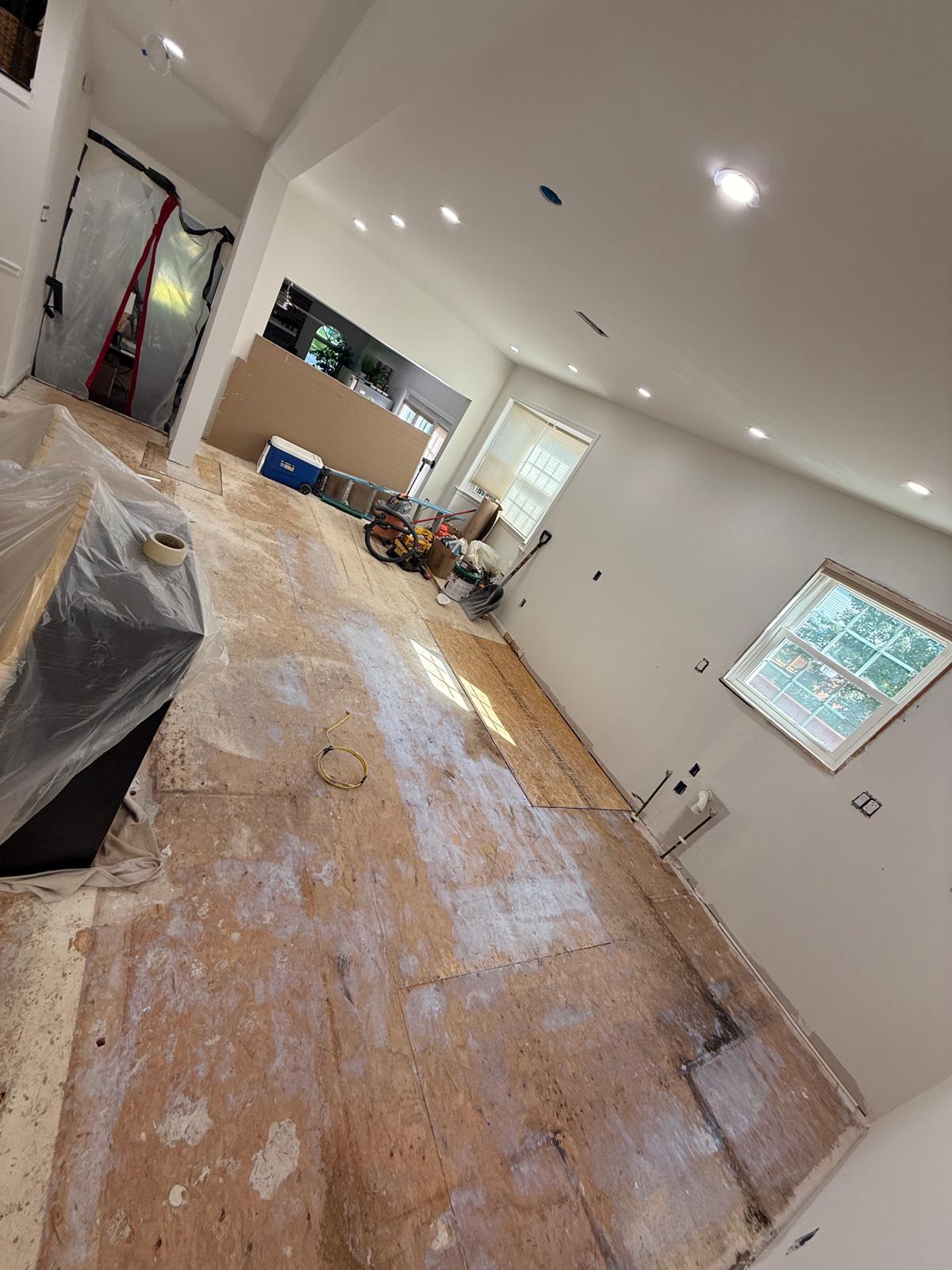 Open-plan room with floor levelling compound applied, doorway sealed with a zip dust barrier and recessed lights on