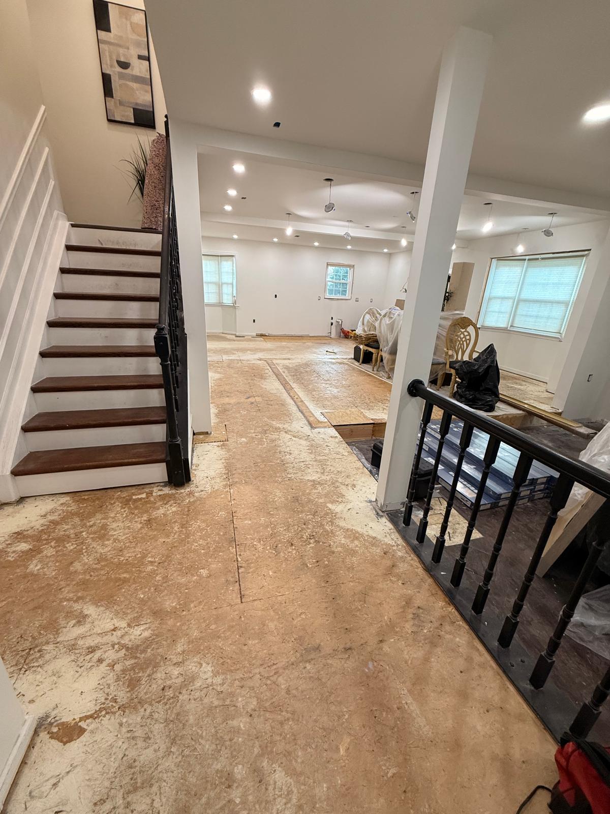 Foyer beside the staircase with floor coverings removed to the underlayment and new flooring staged in the sunken room