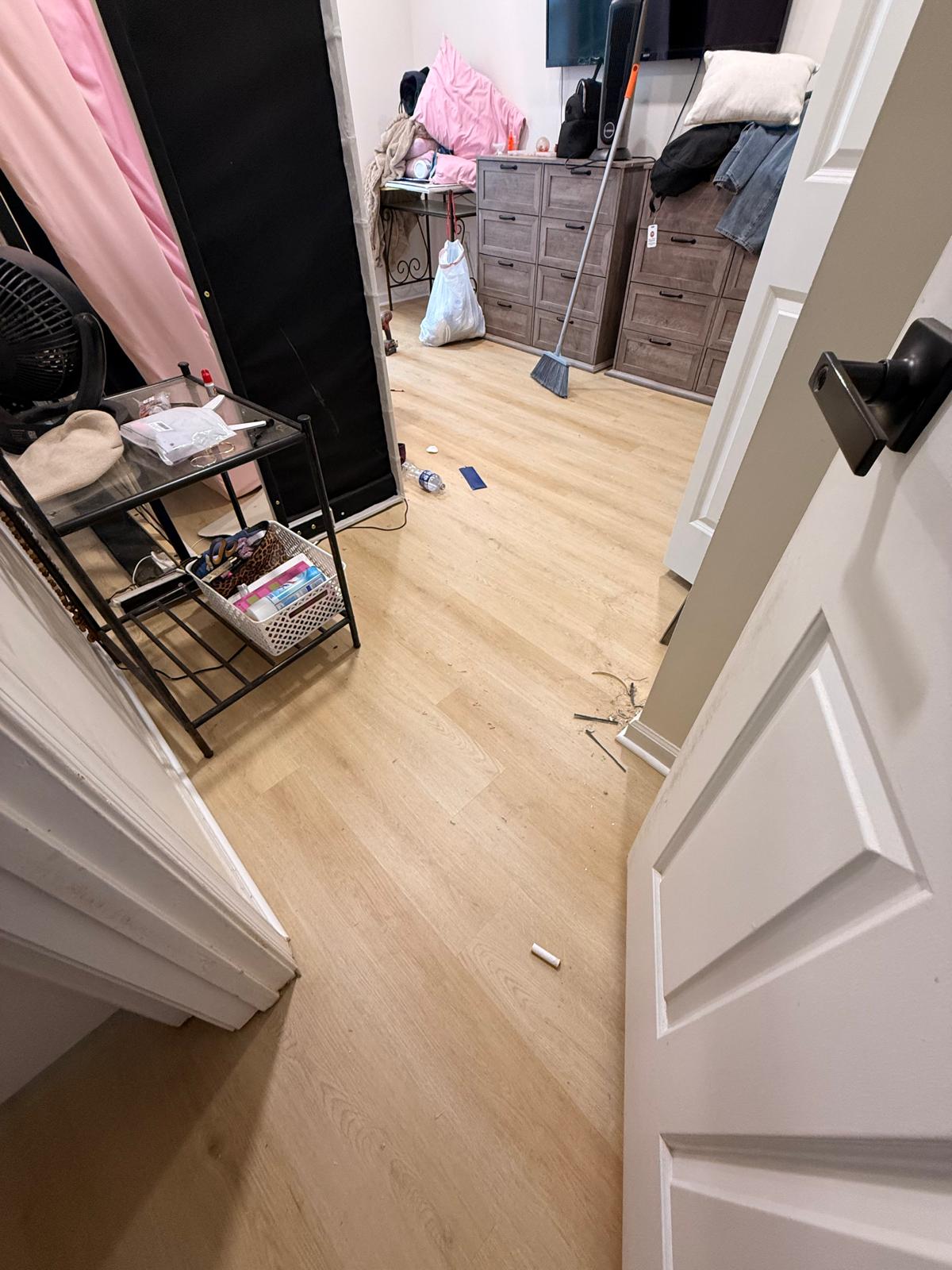 Bedroom with new light oak-tone plank flooring installed and final cleanup under way