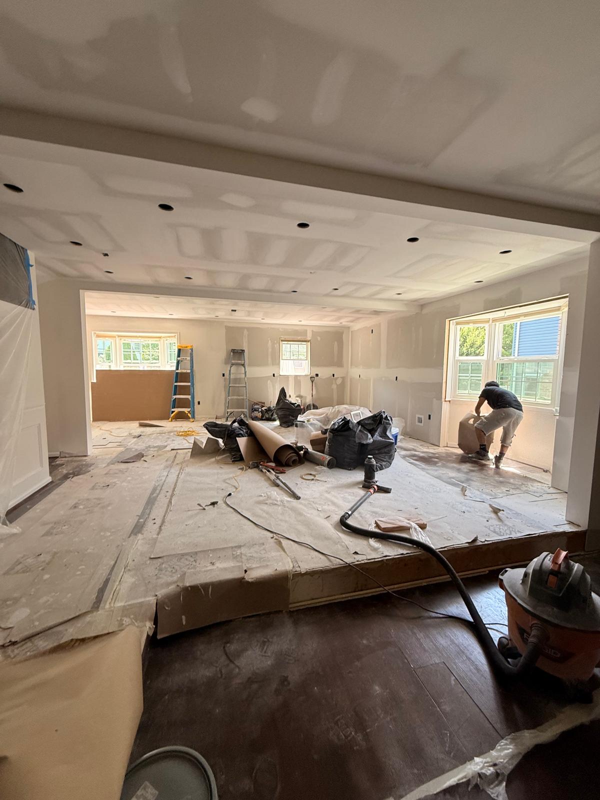 Living and dining area mid-renovation with new drywall taped and joint compound applied across walls and ceiling
